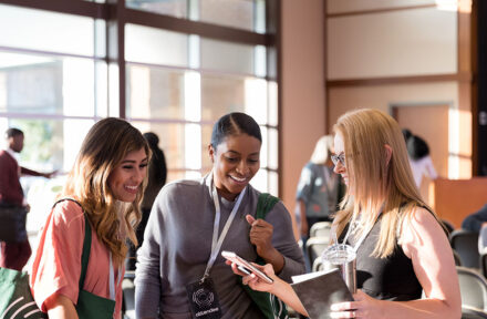 A diverse group of mid adult women attending the expo smile at photos on a smart phone.